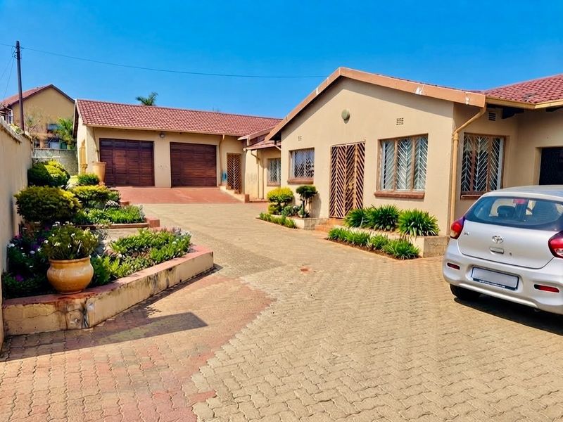 Front view of the property featuring a paved driveway, double garage, and established garden beds with security features on windows and doors.