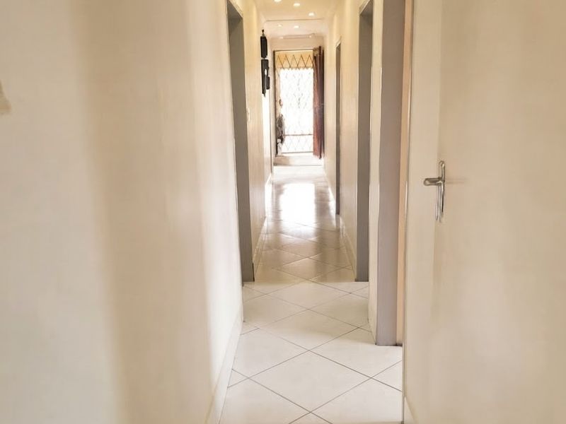 A long, tiled hallway featuring recessed downlighting and multiple doorways leading to adjacent rooms.