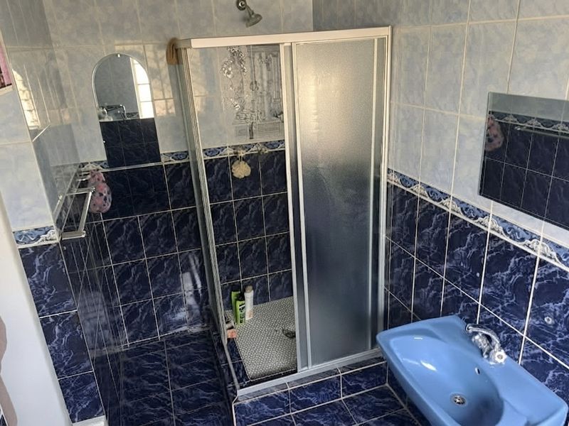 A dated bathroom featuring blue tiled walls and flooring, a corner shower enclosure, and a matching blue wall-mounted basin.