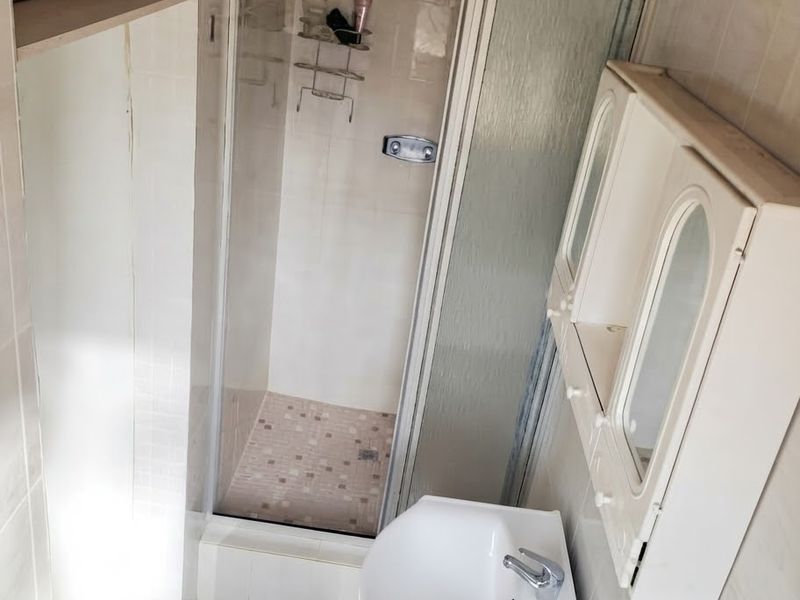 A compact bathroom featuring a shower enclosure, wall-mounted vanity cabinet, and pedestal basin with tiled finishes throughout.