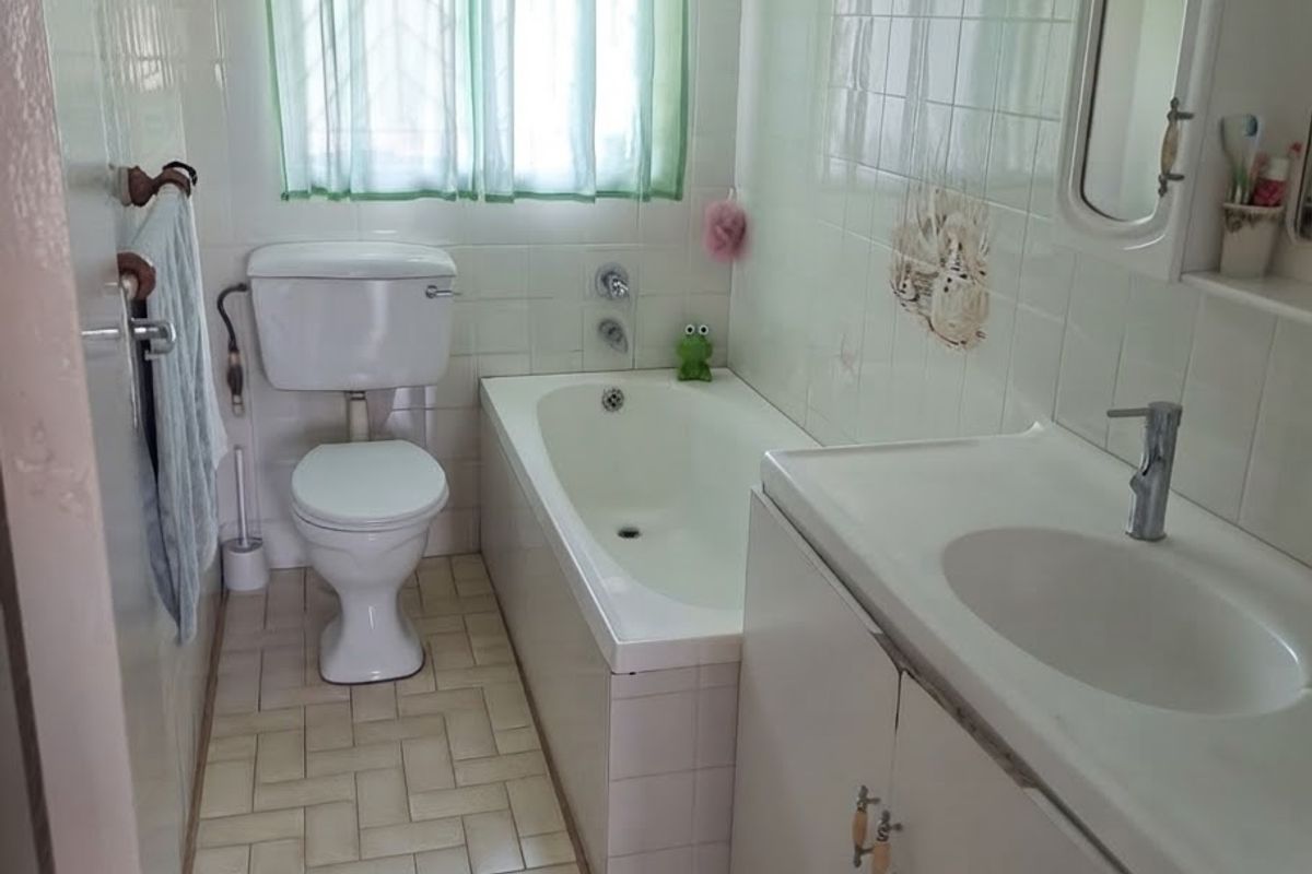 A functional bathroom featuring a bathtub, toilet, and a vanity unit with a built-in washbasin, finished with classic wall and floor tiling.