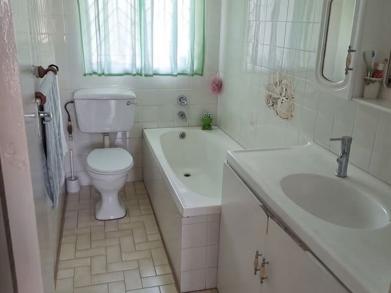 A functional bathroom featuring a bathtub, toilet, and a vanity unit with a built-in washbasin, finished with classic wall and floor tiling.