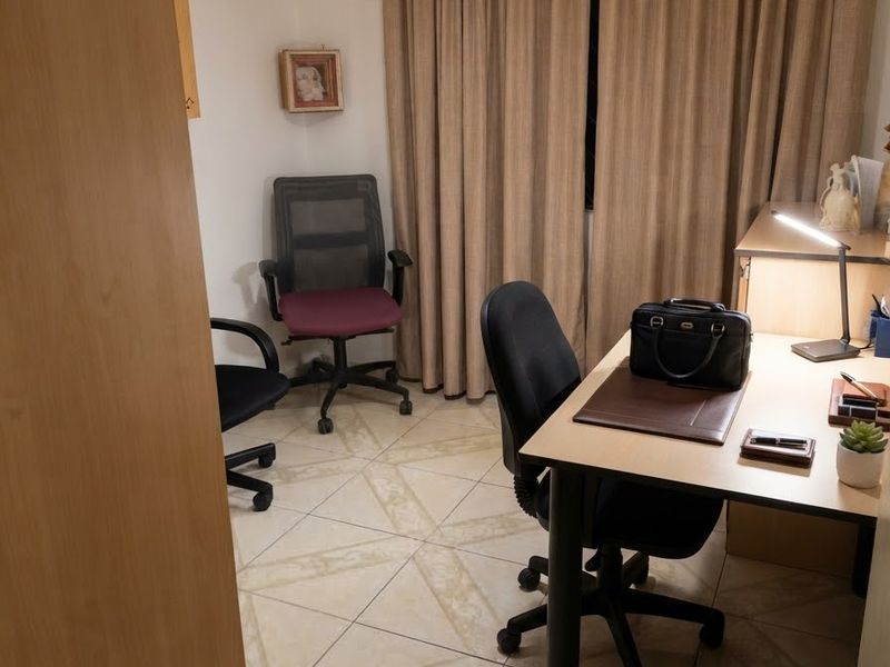 A functional home office space featuring tiled flooring and neutral curtains, providing a quiet area suitable for work or study.