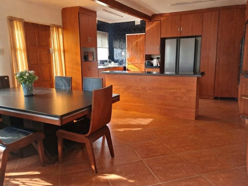 Open-plan kitchen and dining area featuring warm-toned built-in cabinetry, a central kitchen island, and durable tiled flooring throughout the space.