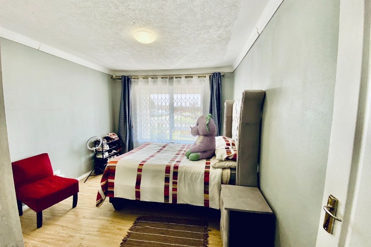 A standard bedroom featuring laminate flooring, a window with a security gate, and decorative ceiling cornicing.