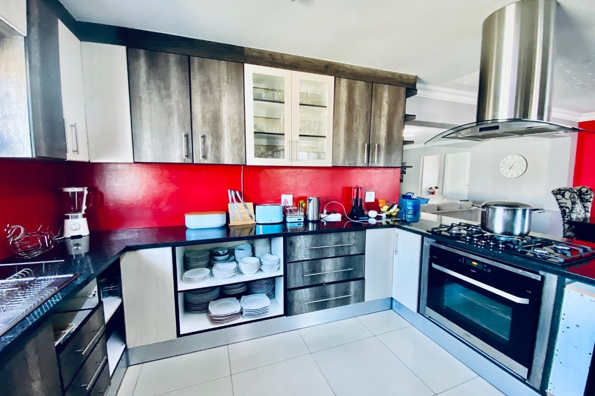 Modern kitchen featuring two-tone cabinetry, stone countertops, a bold red splashback, and integrated stainless steel appliances including a gas cooktop and extractor fan.