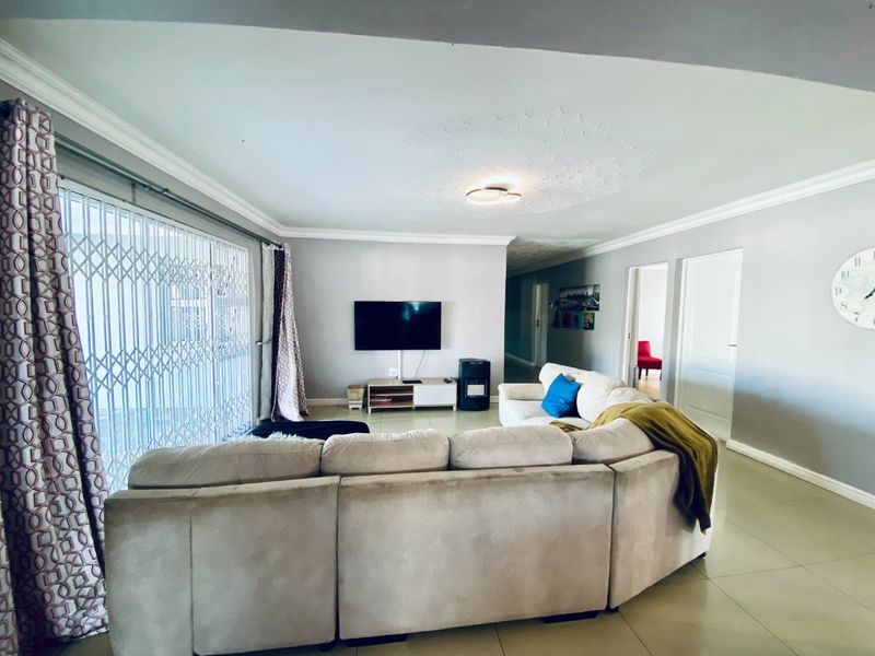 Spacious living room featuring tiled flooring, decorative ceiling rose, coving, and a large sliding door with a security gate leading to the exterior.