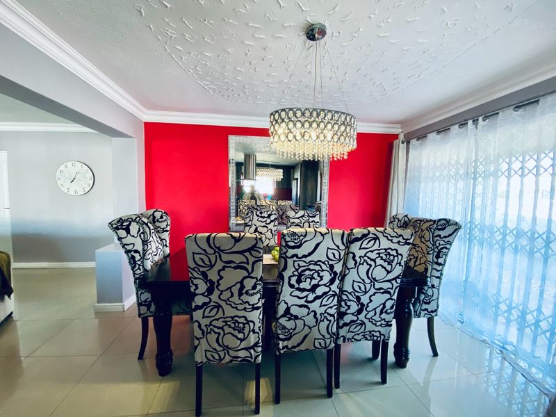 A formal dining room featuring tiled floors, decorative ceiling detailing, and sliding glass doors with security gates, accented by a bold red feature wall.