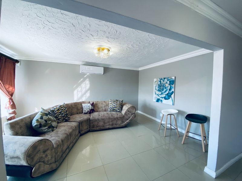 A well-maintained living room featuring neutral tiled flooring, textured ceiling detail, crown molding, and a wall-mounted split-system air conditioner.