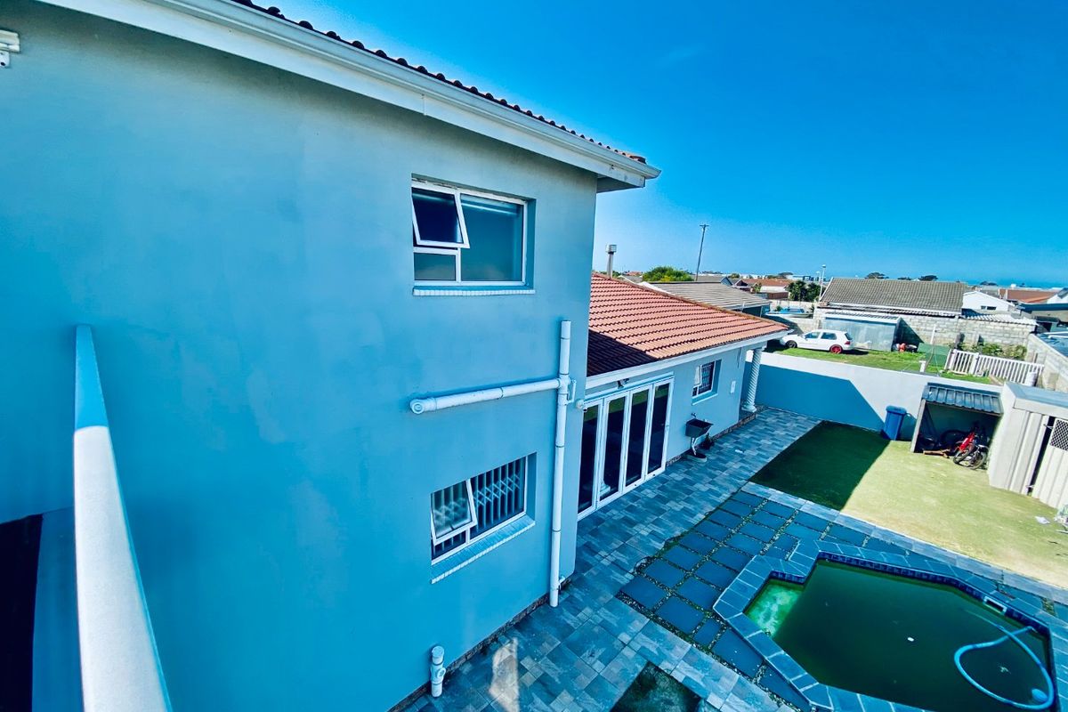 Rear exterior view of the property featuring a paved patio area, swimming pool, and multi-story building facade with tiled roofing.