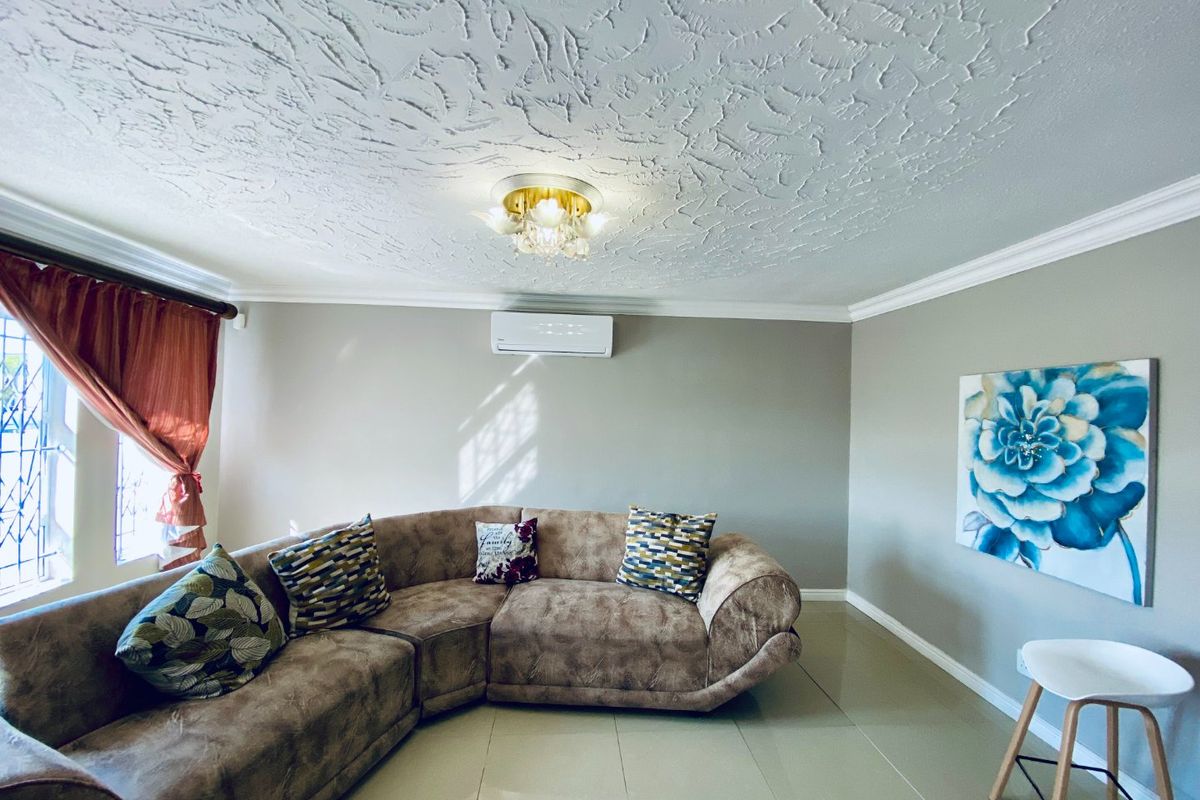 A well-maintained living room featuring tiled flooring, crown molding, a textured ceiling, and a wall-mounted split-system air conditioner.