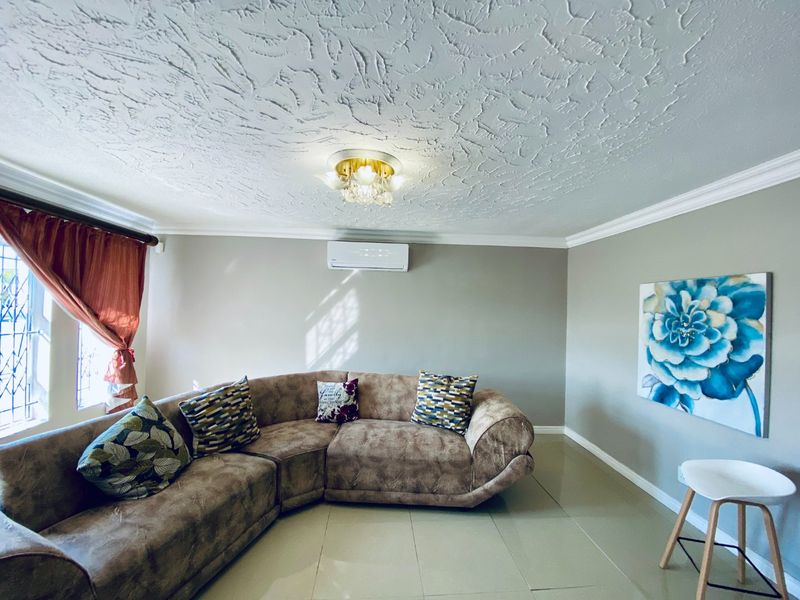 A well-maintained living room featuring tiled flooring, crown molding, a textured ceiling, and a wall-mounted split-system air conditioner.