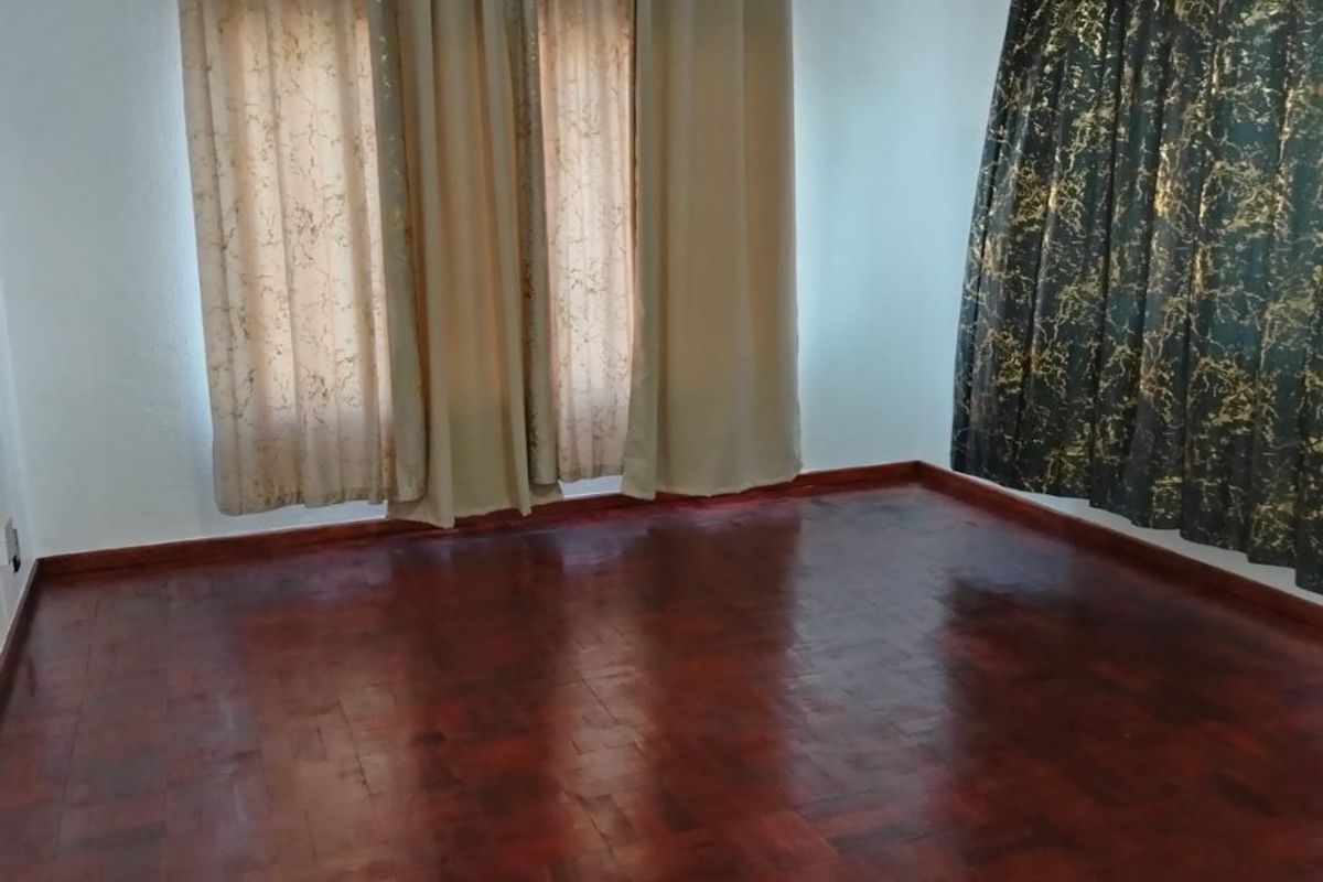 A bright, empty living room featuring polished dark wood parquet flooring and dual window treatments.