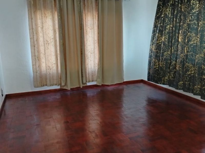A bright, empty living room featuring polished dark wood parquet flooring and dual window treatments.