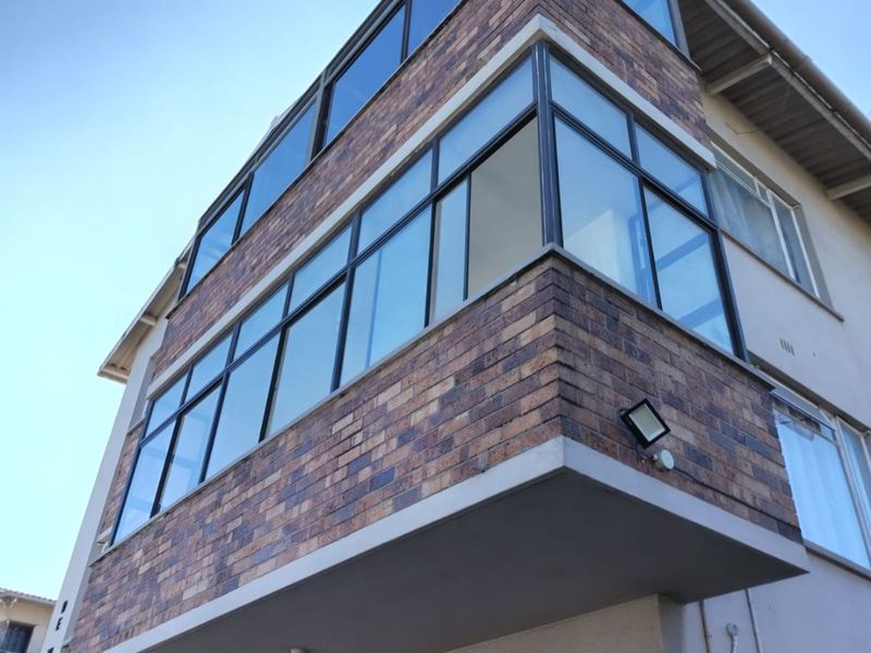 Low angle view of an apartment building facade featuring a prominent enclosed balcony with brick cladding and large aluminum-framed windows.