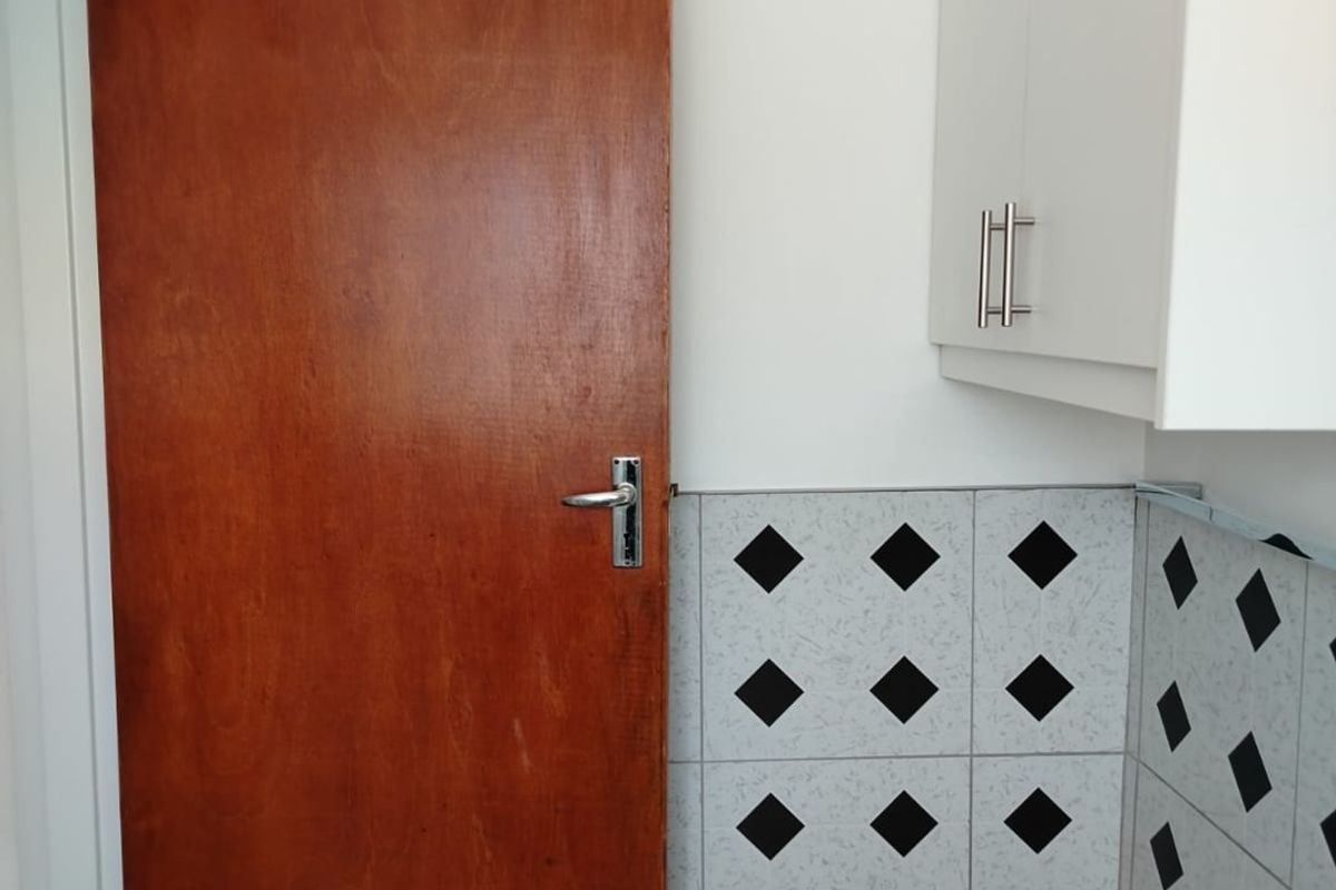 A functional kitchen area featuring white wall-mounted cabinetry and a decorative tiled splashback, providing a clean and practical workspace.