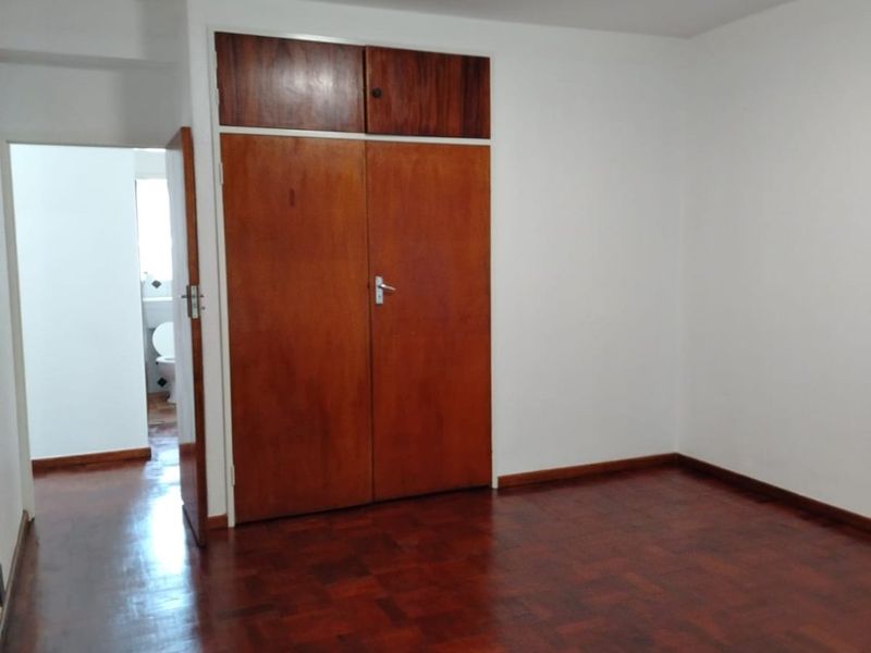 A vacant bedroom featuring classic parquet flooring and built-in wooden cupboards, with an adjacent view into a bathroom area.