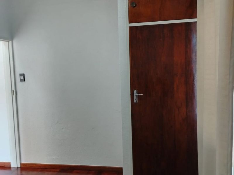 A vacant bedroom featuring original parquet flooring and a built-in wooden cupboard with overhead storage.