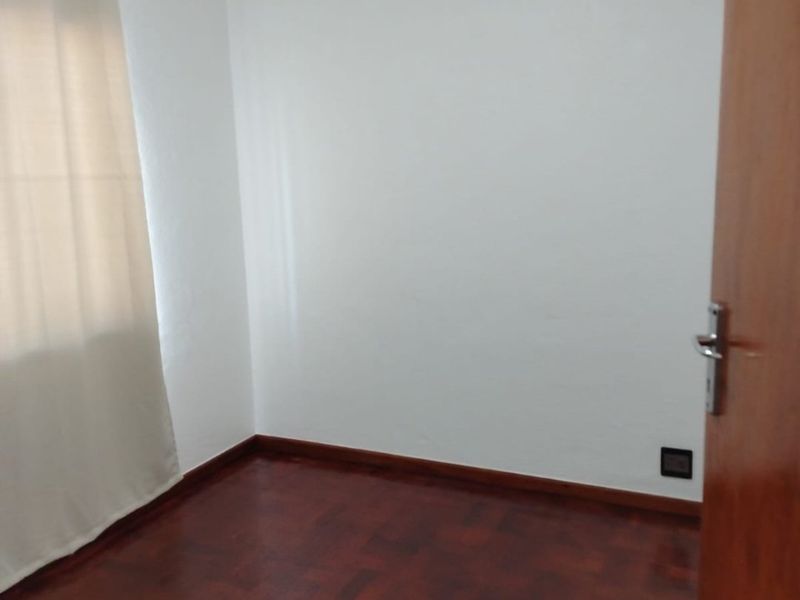 An empty bedroom featuring polished parquet flooring, a ventilation grille, and a timber door, providing a clean and neutral space ready for furnishing.