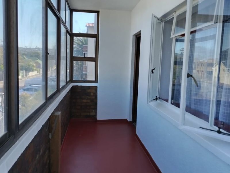 An enclosed balcony featuring exposed brickwork, large windows providing natural light, and a painted concrete floor.