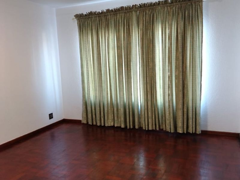 A spacious, empty bedroom featuring classic dark parquet flooring and neutral white walls, ready for personalization.