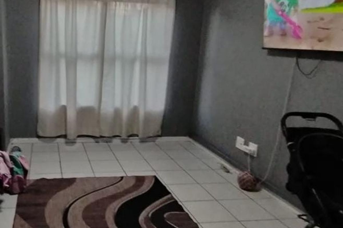A living room featuring tiled flooring, neutral grey walls, and a ceiling light fixture, providing a functional and simple living space.