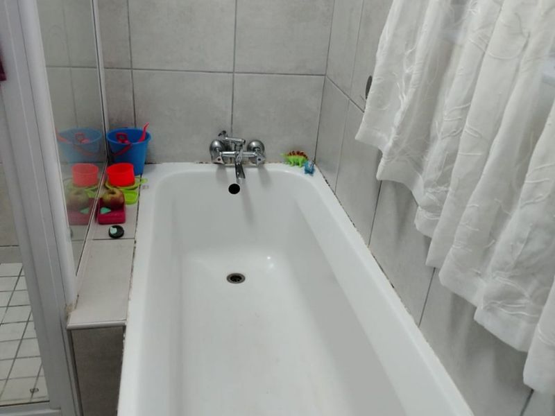 A functional bathroom featuring a standard bathtub with a shower screen and tiled walls with a decorative border.