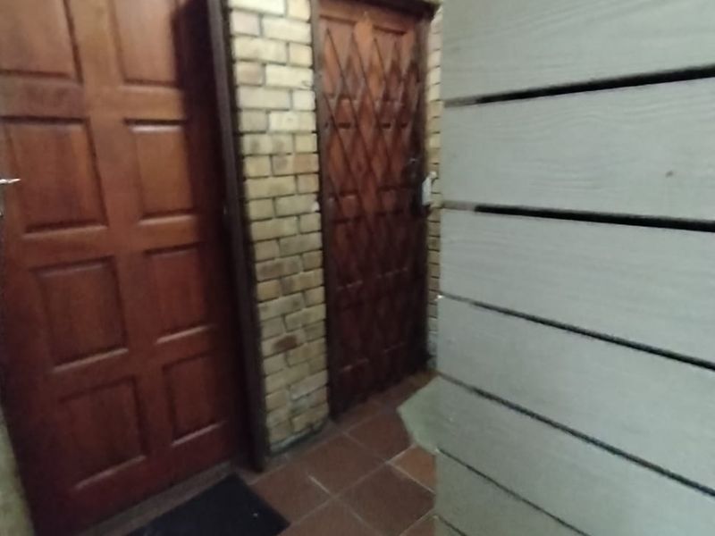 An entrance area featuring exposed brick walls, tiled flooring, and wooden doors with security gates.