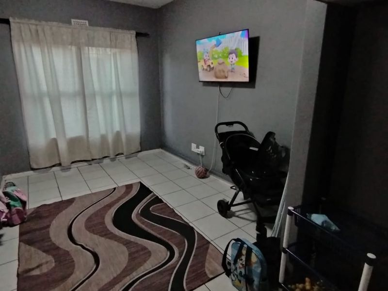 A living room area featuring tiled flooring, neutral grey walls, and a wall-mounted television point.