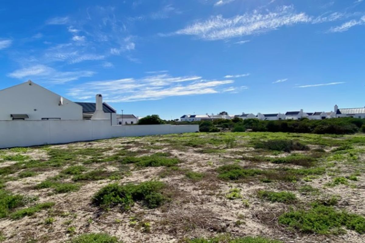 A vacant residential plot featuring natural ground cover, enclosed by a boundary wall, situated within a developed residential estate.