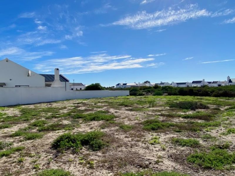 A vacant residential plot featuring natural ground cover, enclosed by a boundary wall, situated within a developed residential estate.