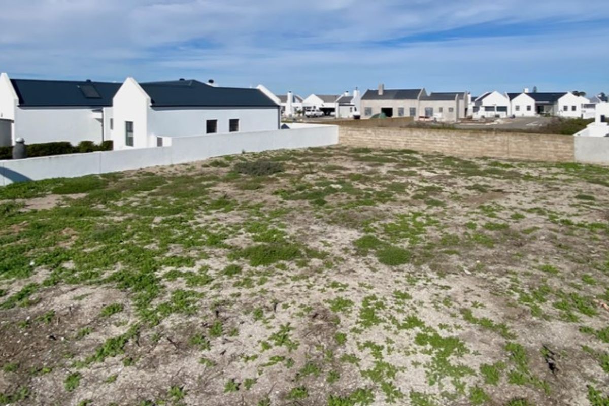 A vacant residential plot featuring sandy ground and perimeter boundary walls, situated within a developed residential estate.