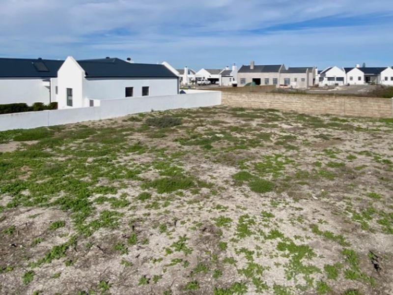 A vacant residential plot featuring sandy ground and perimeter boundary walls, situated within a developed residential estate.