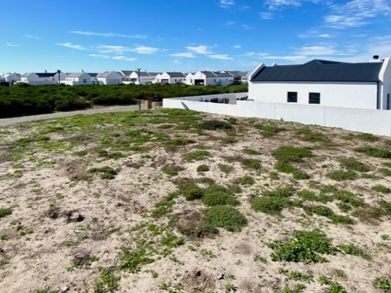 A vacant residential plot of land featuring natural vegetation and a boundary wall, situated within a developed residential estate.