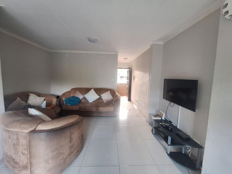 A living room featuring neutral tiled flooring and plain walls, providing a functional and open space with direct access to the entrance.
