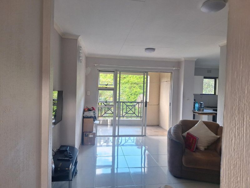 Open plan living area featuring tiled flooring and a sliding glass door leading to a balcony, with an adjacent kitchen area.