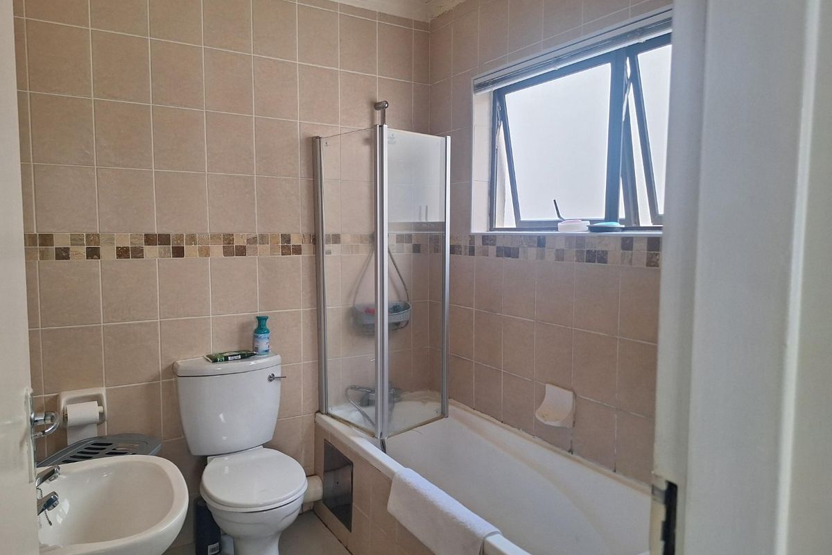 A functional bathroom featuring a shower-over-bath combination, pedestal basin, and toilet, finished with neutral wall and floor tiling.