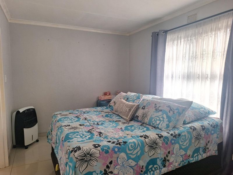 A bedroom featuring tiled flooring and a window with curtain treatments, providing a functional and neutral living space.
