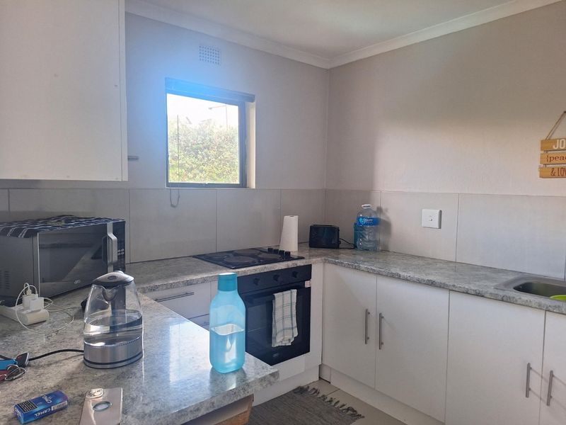 A functional kitchen featuring white cabinetry, granite countertops, a built-in oven, and an electric hob with a tiled backsplash.