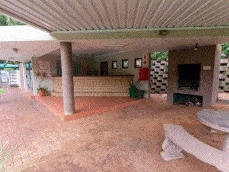 A covered outdoor patio area featuring a built-in braai, brick paving, and structural support columns, suitable for outdoor entertaining.