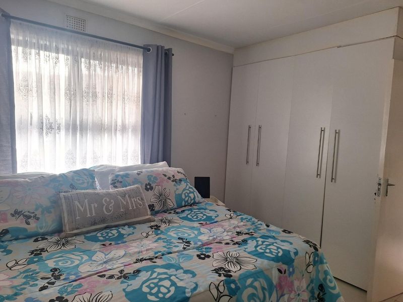 A functional bedroom featuring built-in cupboards and a window with natural light, providing a clean and practical living space.