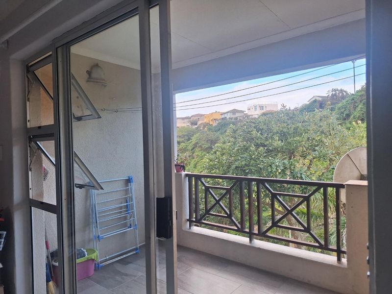 A covered balcony featuring tiled flooring and a wooden balustrade, offering an elevated view of the surrounding neighborhood and greenery.