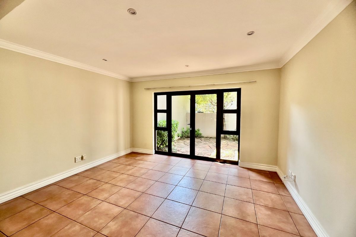 A bright, empty living room featuring neutral walls, tiled flooring, recessed lighting, and large glass doors providing direct access to a private outdoor area.