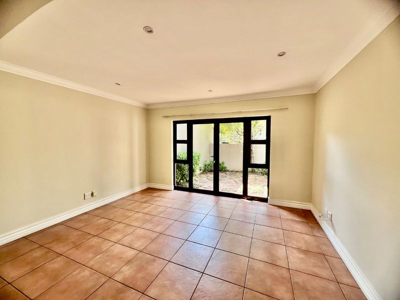A bright, empty living room featuring neutral walls, tiled flooring, recessed lighting, and large glass doors providing direct access to a private outdoor area.