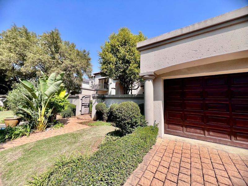Front exterior view of the property featuring a paved driveway, a secure garage, and a well-maintained landscaped garden with a pedestrian gate.