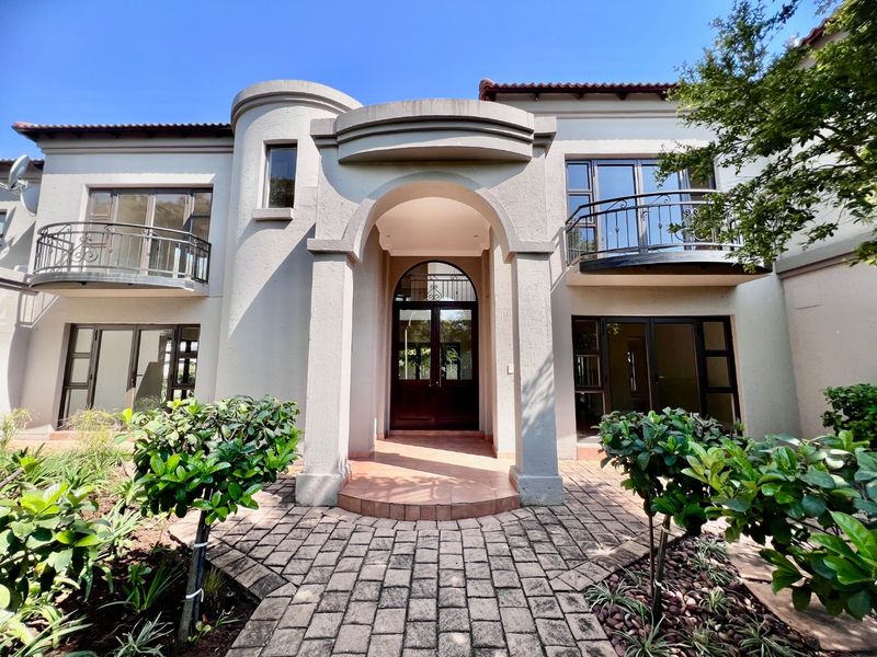 A well-maintained double-storey home featuring an arched portico entrance, wrought iron balconies, and a paved front garden walkway.