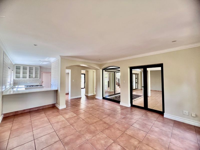 Spacious open-plan living area featuring tiled floors, neutral walls, and a seamless flow into the kitchen, with large glass doors leading to an internal courtyard.