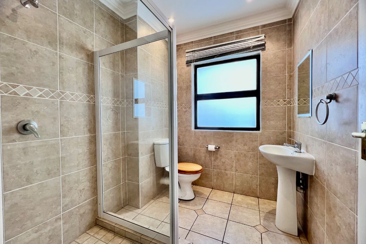 A clean, well-maintained bathroom featuring a pedestal basin, toilet, and a glass-enclosed shower with neutral floor-to-ceiling tiling.