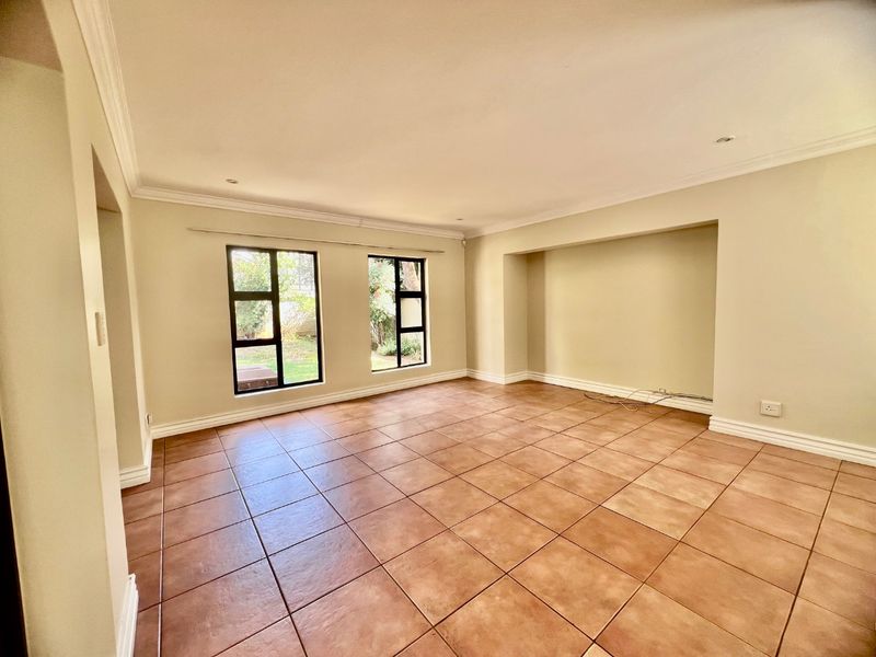 A spacious, empty living room featuring neutral walls, tiled flooring, recessed lighting, and a built-in alcove with views of the garden.