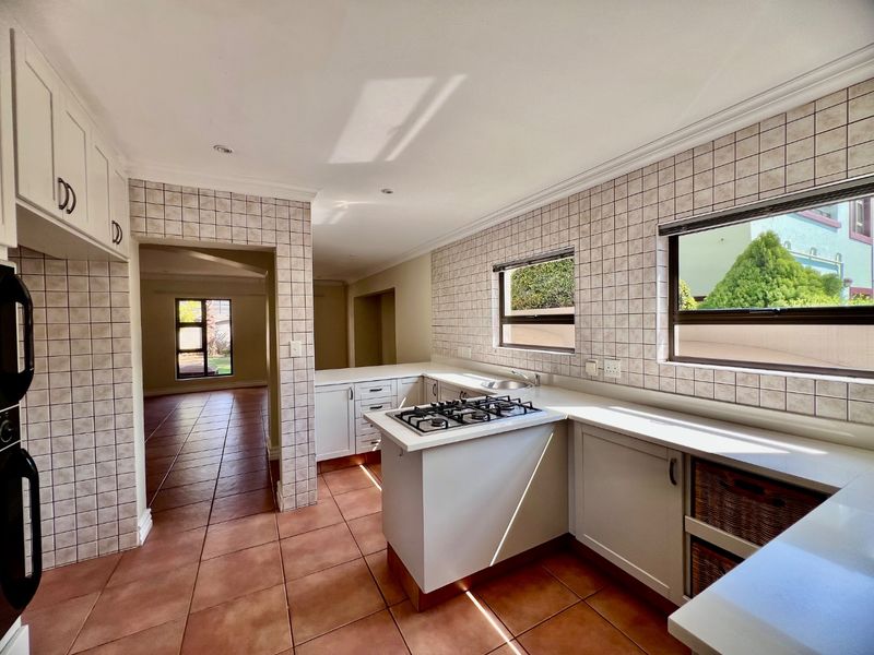 A functional kitchen featuring tiled flooring, a gas hob, built-in cabinetry, and a tiled splashback, with an open flow to the adjacent living area.